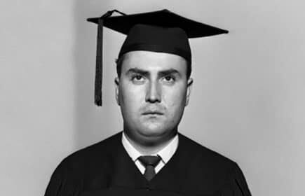 A black and white photo of a man in a graduation gown, representing college graduates and their financial regrets to avoid.