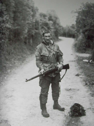 Forrest Guth WWII soldier holding rifle on dirt road.