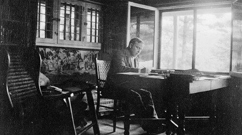 An old photo depicting a man engrossed in his habit of diligently writing in his diary while sitting at a desk.
