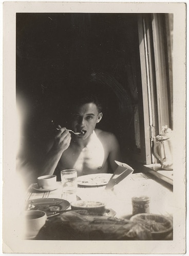 Vintage young man eating fork in mouth at table.