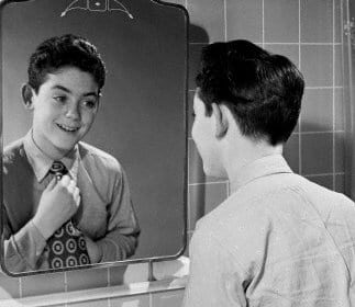 A young child looking at himself in the mirror.