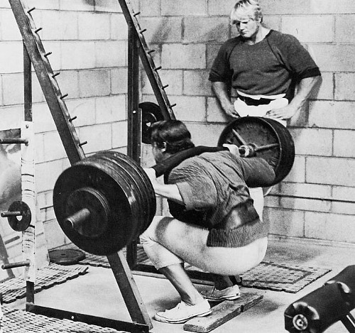 Vintage man deadlifting huge barbell in gym.