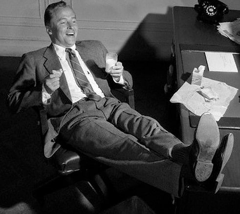 Vintage businessman leaning back in desk chair at work.