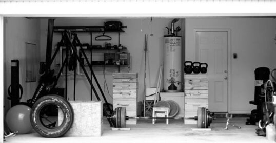 A black and white photo of a garage turned into a home gym, filled with equipment.