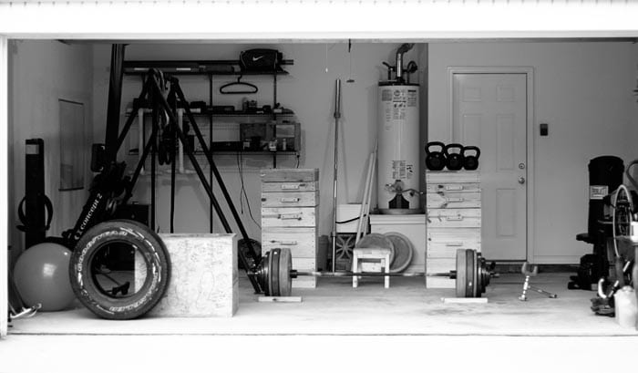 A black and white photo of a garage turned into a home gym, filled with equipment.