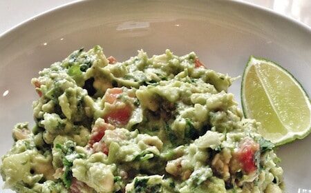 A man's-man guacamole recipe served on a white plate with lime wedges.