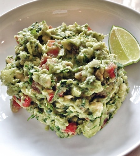 A man's-man guacamole recipe served on a white plate with lime wedges.
