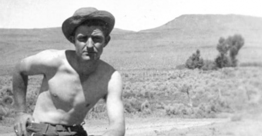 A tough man in a hat posing on a dirt road.