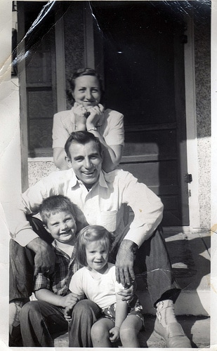 Famille vintage avec 2 enfants assise devant la maison.