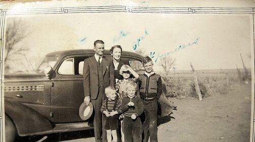 An old photo of a family posing in front of a car, trying to figure out how to fit their children inside.