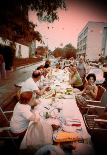 Vintage block party people eating dinner talking long picnic tables.