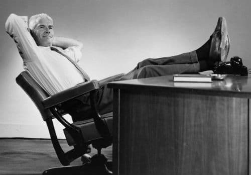 hombre de negocios vintage inclinado hacia atrás en los pies de la silla en el escritorio 
