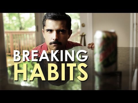 A man with a mustache examining a can labeled "breaking habits" through a video.