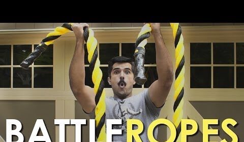 A man is performing Wind Sprints while holding a Battle Rope in front of a garage.