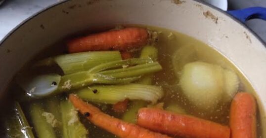 A pot with carrots, celery, and onions simmering in it for a flavorful stock or soup.