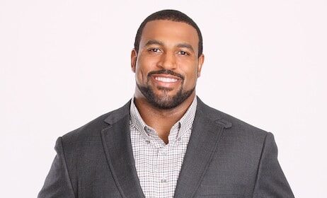 A man in a suit holding a football, possibly a NFL player.