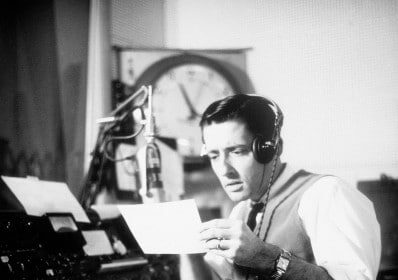 A man in a radio studio reading a letter for his podcast on the Art of Manliness.