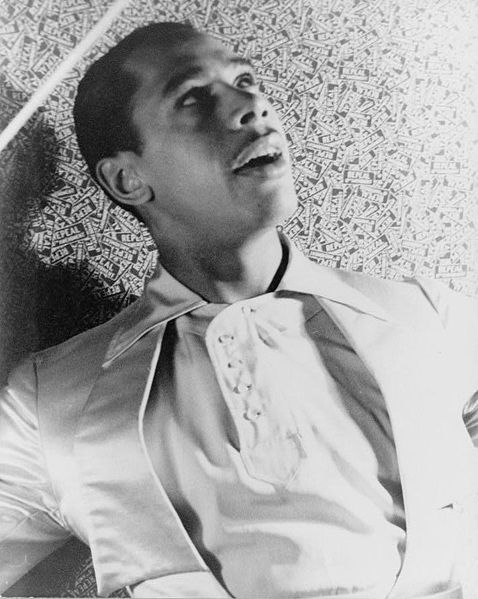 A hep black and white photo of Cab Calloway jiving on the floor.