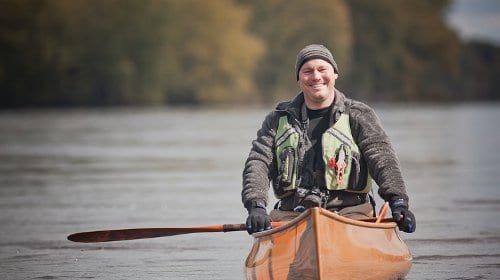 An outdoor shop owner is paddling a canoe in a river.