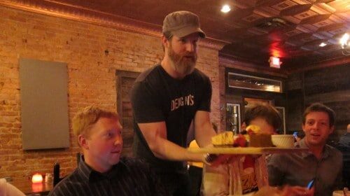The restaurant owner is holding a tray of food in front of a group of people.