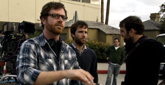 A group of men standing on a street in front of a camera with a film director overlooking the job.