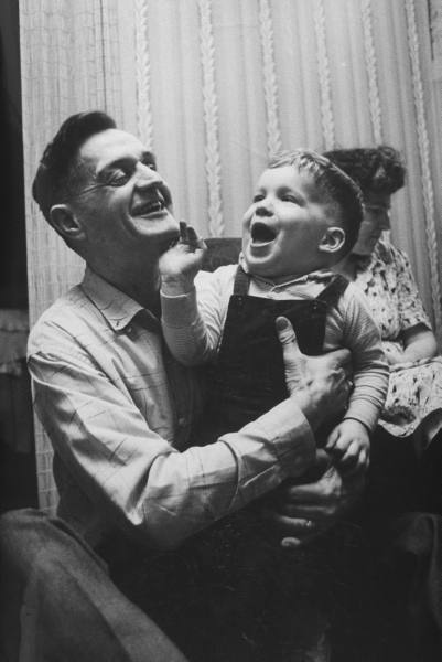 An old black and white photo of a man holding a child, depicting tenderness and care.