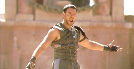 A man in a Roman costume embodying lessons in manliness as a gladiator, solemnly gripping a sword.