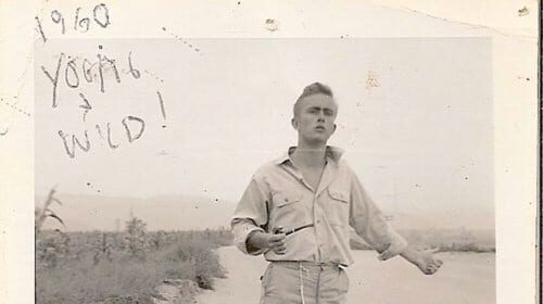An old photo of a man hitchhiking on a dirt road in the USA.