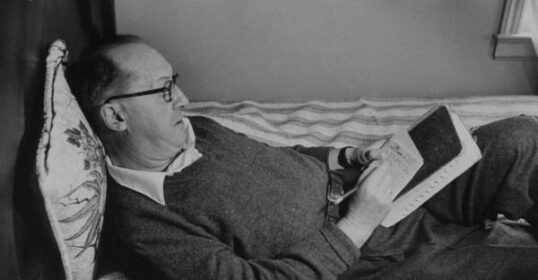 A man taking 30 days to start a journal in bed, reading a book.