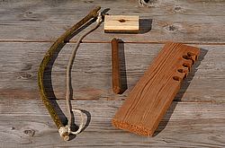 A wooden bird feeder and a wooden stick on a wooden table, evoking a sense of traditional firestarting.