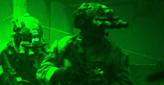 A group of soldiers in camouflage gear in a dark room pulling an all-nighter.