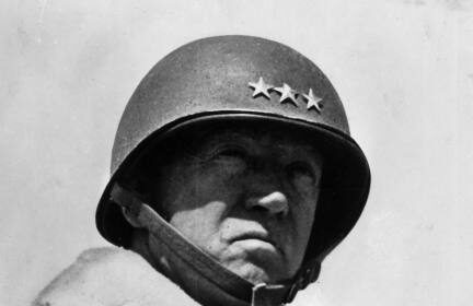 A black and white photo of a man wearing a George S. Patton helmet.