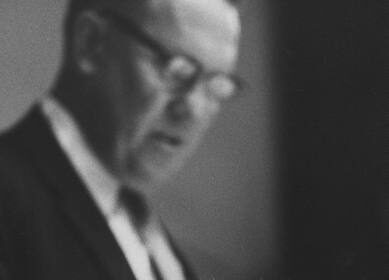 A man in a suit and tie is sitting next to a man in a suit, giving him praise.