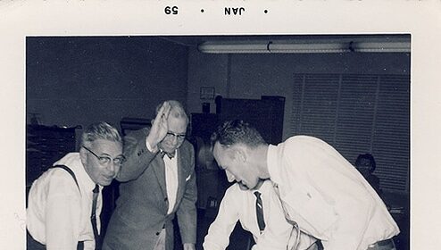 A group of men standing around a table, discussing how to ask for a raise.