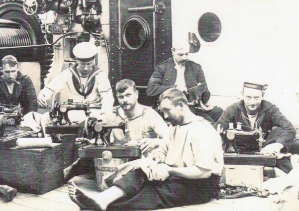 A group of men sitting on the floor of a ship, sewing.