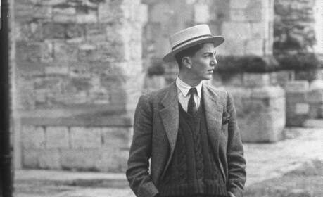 A gentleman in a suit and hat standing on a cobbled street.