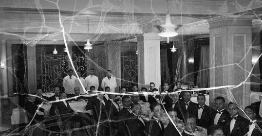 A black and white photo capturing a group of people engaged in a shared ritual, exuding an aura of power within the room.