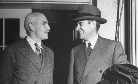 Two men in suits and hats strategizing at a meeting.