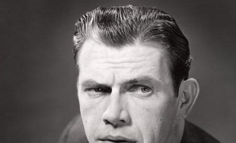 A man posing with his hand on his chin, captured in a black and white photo.