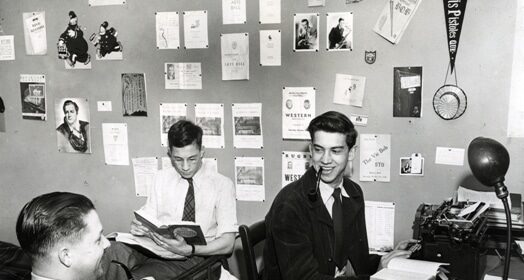 Three men testing out a moneyball strategy at a desk with a typewriter in front of them.