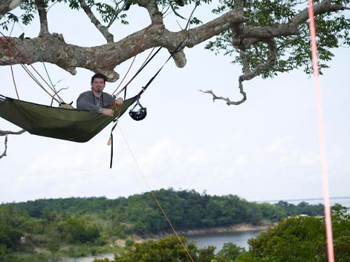 Man in tree hammock hanging from large tree branch.