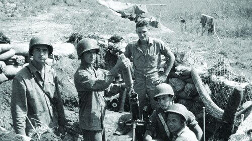 A group of men in uniform standing next to a pile of dirt, conducting a WWII case study.