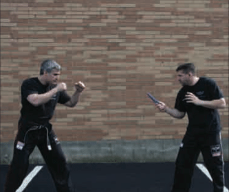 Two men practicing Krav Maga techniques and defending themselves in a parking lot.