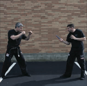 Two men practicing Krav Maga techniques and defending themselves in a parking lot.