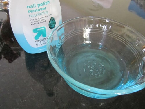 Bottle of nail polish remover with a bowl placed at table.