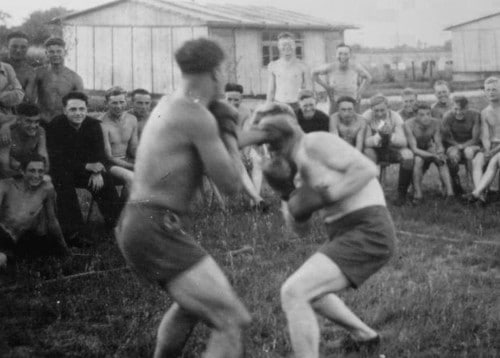 Vintage men boxing in grass yard field with onlooking action shot.