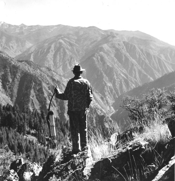 A man standing on top of a mountain with his own rifle for survival reasons.