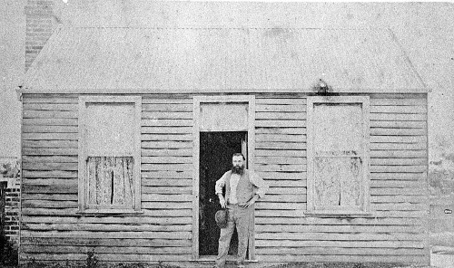 Vintage man standing in doorway of cabin home.