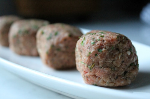 Raw meatballs lined up on plate to be cooked.