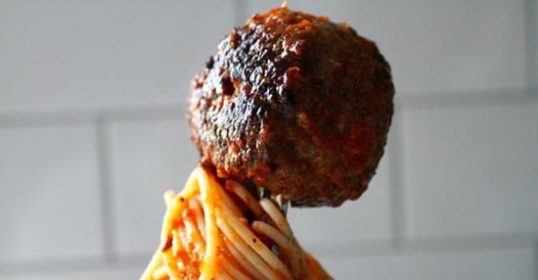 A person is holding a delicious meatball on a fork.